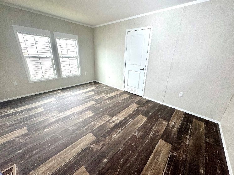 Empty room with wood-look flooring, white walls, and a white door. Two windows are on the left.
