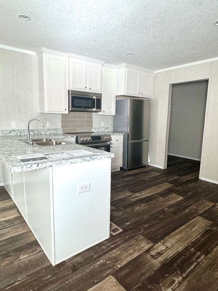 White kitchen with stainless steel appliances, granite countertops, and dark wood flooring.