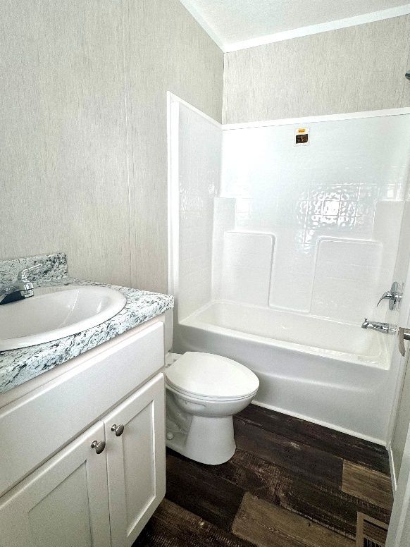 Bathroom with white vanity, toilet, and shower/tub combo. Dark wood-look flooring and light gray textured walls.