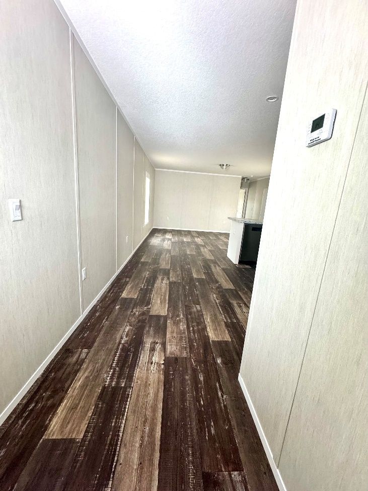 Long, narrow room with wood-look flooring, white walls, and a view towards a kitchen area.