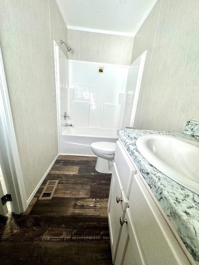 Bathroom with white shower, toilet, and vanity. Brown, wood-look flooring.