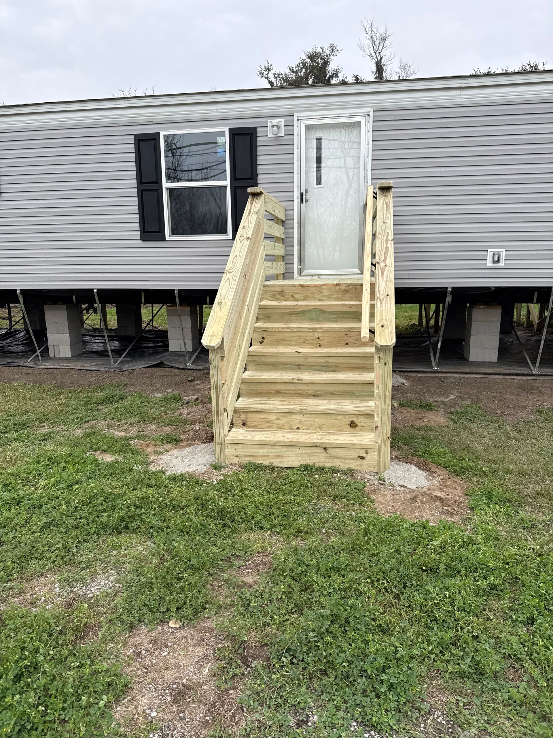 A mobile home with a wooden deck and stairs in front of it.
