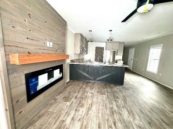 Living area with a fireplace, kitchen, and wood-look flooring. The fireplace has a wooden mantle.