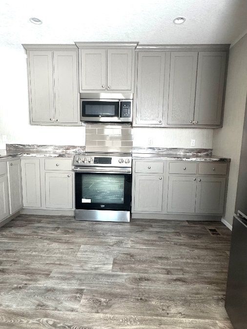 Light gray kitchen with matching cabinets, countertops, and appliances.  A microwave is over the stove.  The floor is gray wood-look.