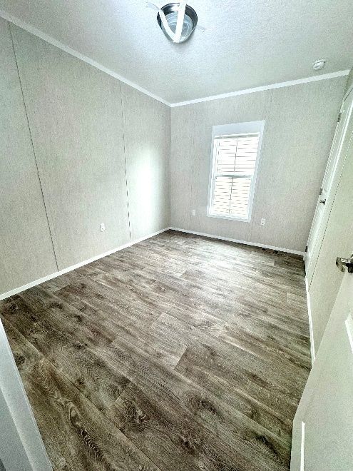 Empty bedroom with wood-look flooring, a window, and white walls. A ceiling light fixture is visible.