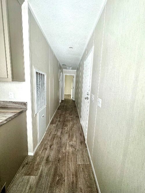 Long, narrow hallway with light-colored walls and wood-look flooring. A doorway is visible at the end.