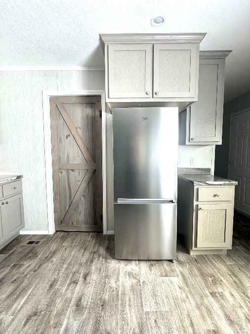 A kitchen with a stainless steel refrigerator, light-colored cabinets, and a wooden sliding door. The flooring is light wood-grain.