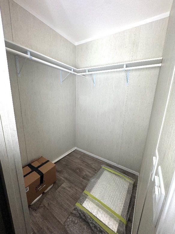 A small, empty walk-in closet with two white rods for hanging clothes. There is a box and a wrapped item on the floor.