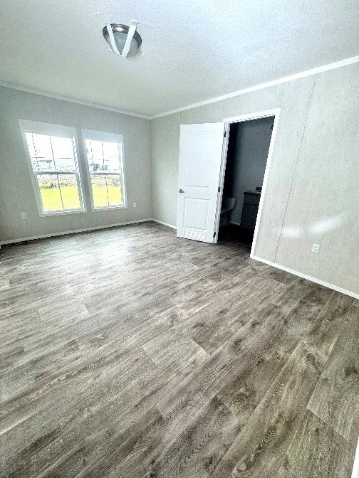 Empty room with gray wood-look flooring, white walls, and a doorway leading to a bathroom. Two windows let in natural light.