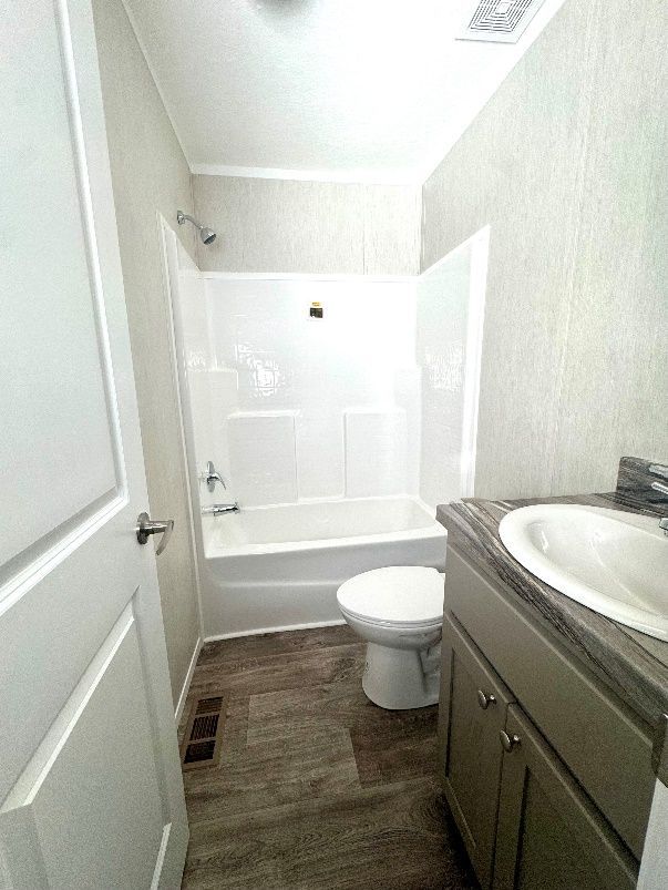 Small bathroom with a white bathtub and shower combo, toilet, and vanity with a sink. The floor is wood-look and the walls are light.