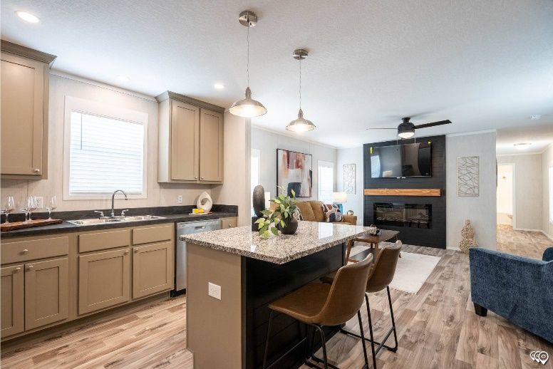Open-concept kitchen and living room with a kitchen island, fireplace, and modern furniture. The kitchen has light brown cabinets and the living room features a blue couch.