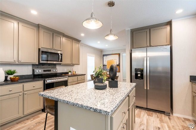 A modern kitchen with light brown cabinets, stainless steel appliances, a granite island, and pendant lights.