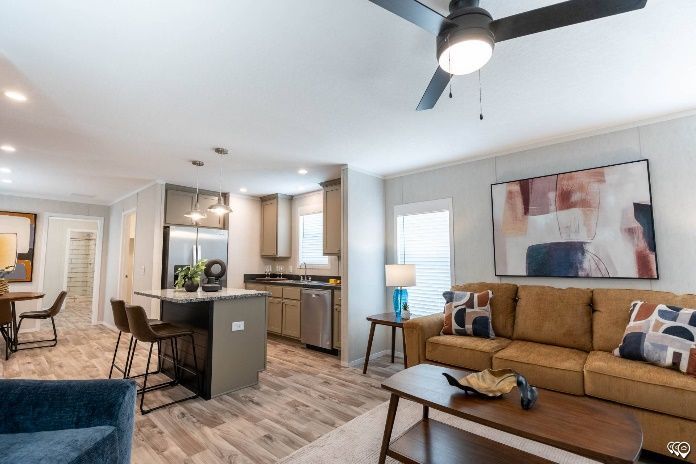 Open-concept living space with kitchen and living room. Brown sofa, kitchen island with stools, and artwork on the walls.