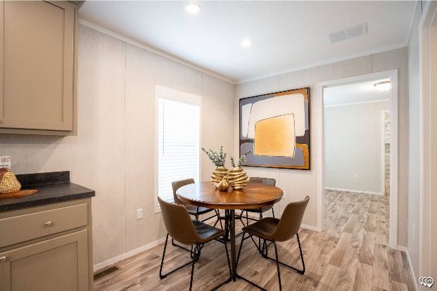 Dining area with a round wooden table, four chairs, and an abstract painting on the wall. Light-colored cabinets are on the left.