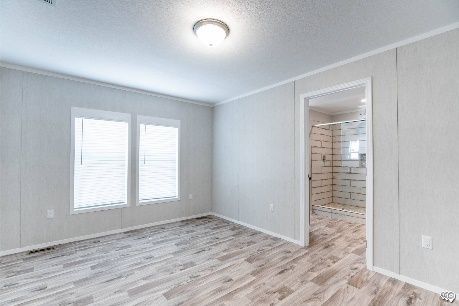 Empty bedroom with light wood-look flooring, two windows with blinds, and a doorway leading to a bathroom with a tiled shower.