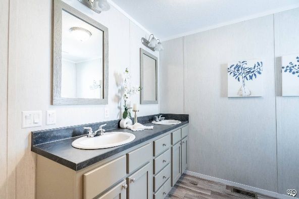 A bathroom with a double vanity, two mirrors, and blue-toned artwork. The walls are white, and the countertops and cabinets are gray.