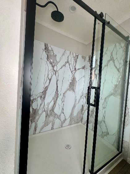 A modern shower stall with a black-framed sliding glass door. The walls are white with a marble-like brown pattern.