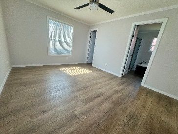 Empty bedroom with light wood-look flooring, gray walls, and a window with blinds. A doorway leads to another room.