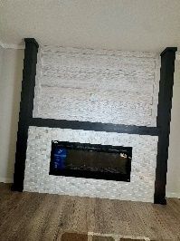 Fireplace with a black frame, a black firebox, white stone surrounding, set in a room with wood flooring and white walls.
