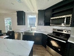 A modern kitchen with dark cabinets, stainless steel appliances, and a marble countertop. A window provides natural light.