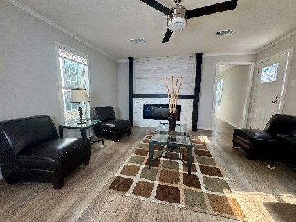 Living room with fireplace, two black leather armchairs, and a patterned rug. A ceiling fan hangs above.