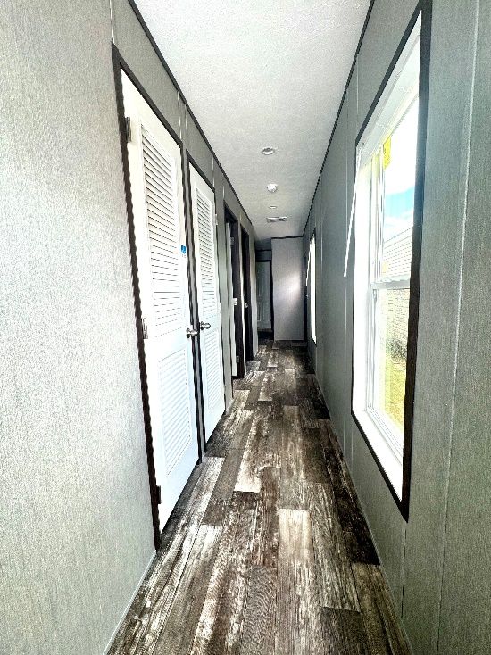 Narrow hallway with a wood-look floor, doors on the left, and a window on the right. The walls are gray.