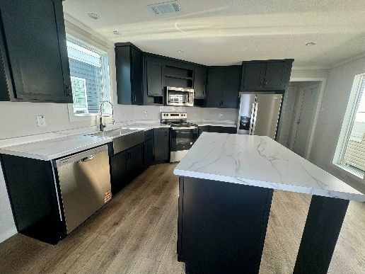 Modern kitchen with black cabinets, white countertops, and an island with a marble-look surface. Stainless steel appliances and light wood flooring.