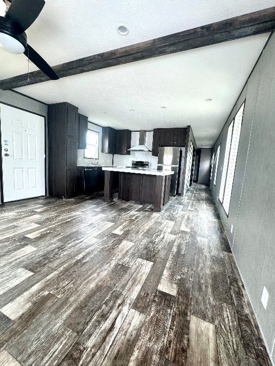 Interior view of a modern home with dark wood cabinets, a kitchen island, and a light-colored floor. The open-plan space has a ceiling fan and ample natural light.