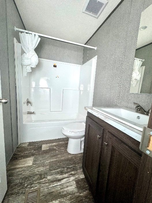 Bathroom with white tub/shower combo, toilet, dark wood vanity, and gray walls. Dark flooring.