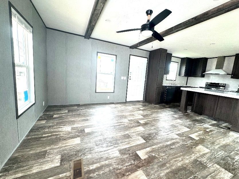 An open-concept living space with wood-look flooring. It has gray walls, a kitchen with dark cabinets, and a ceiling fan.