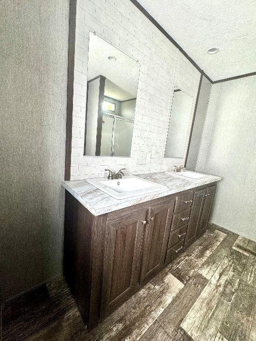 Bathroom with double vanity, two mirrors, and a dark brown cabinet. White countertop with gray and brown faux wood floors.