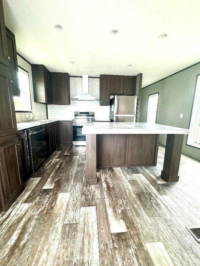 Kitchen with dark brown cabinets, stainless steel appliances, and a large island. Wood-look flooring and white countertops.