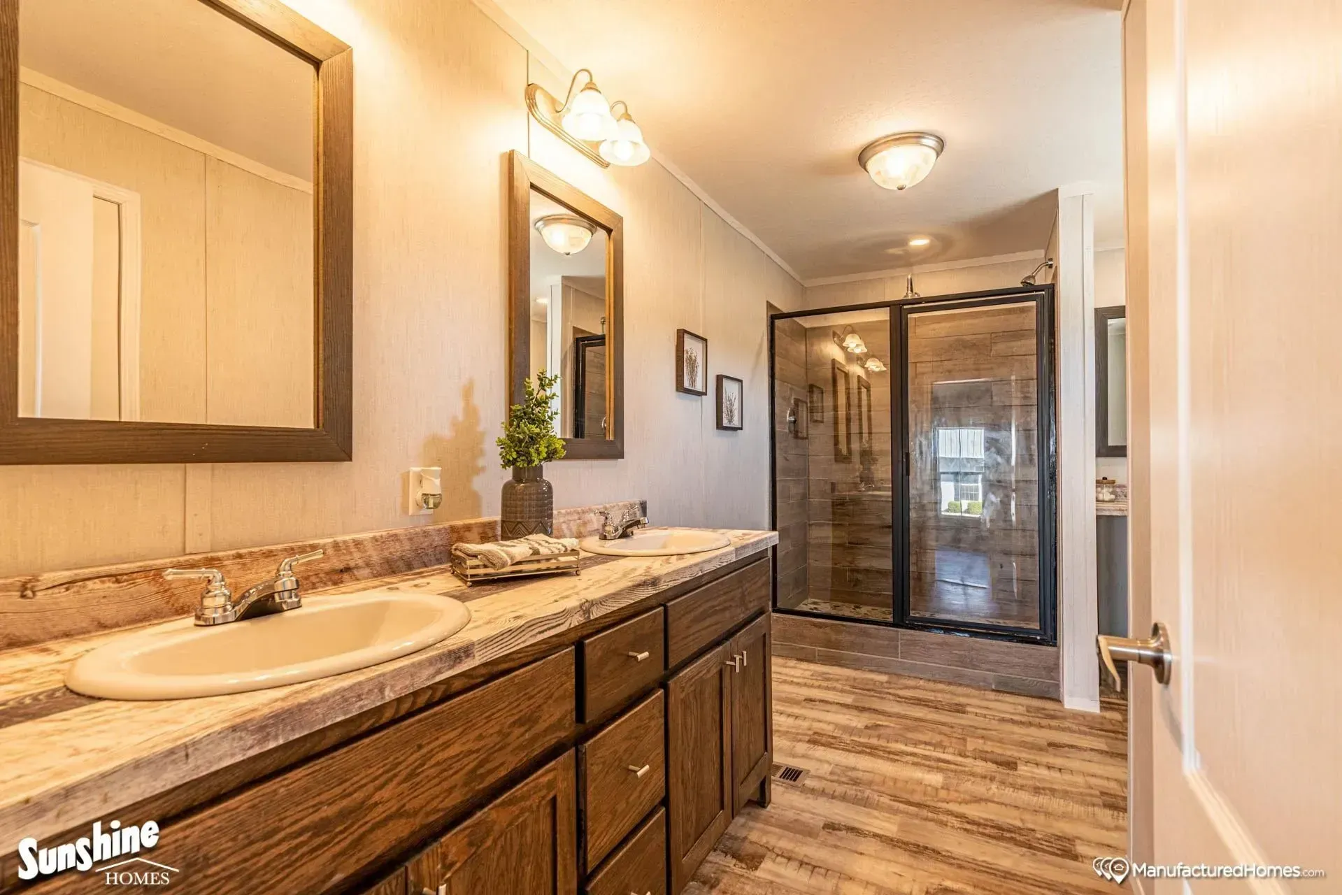 A bathroom with two sinks, two mirrors, and a walk in shower
