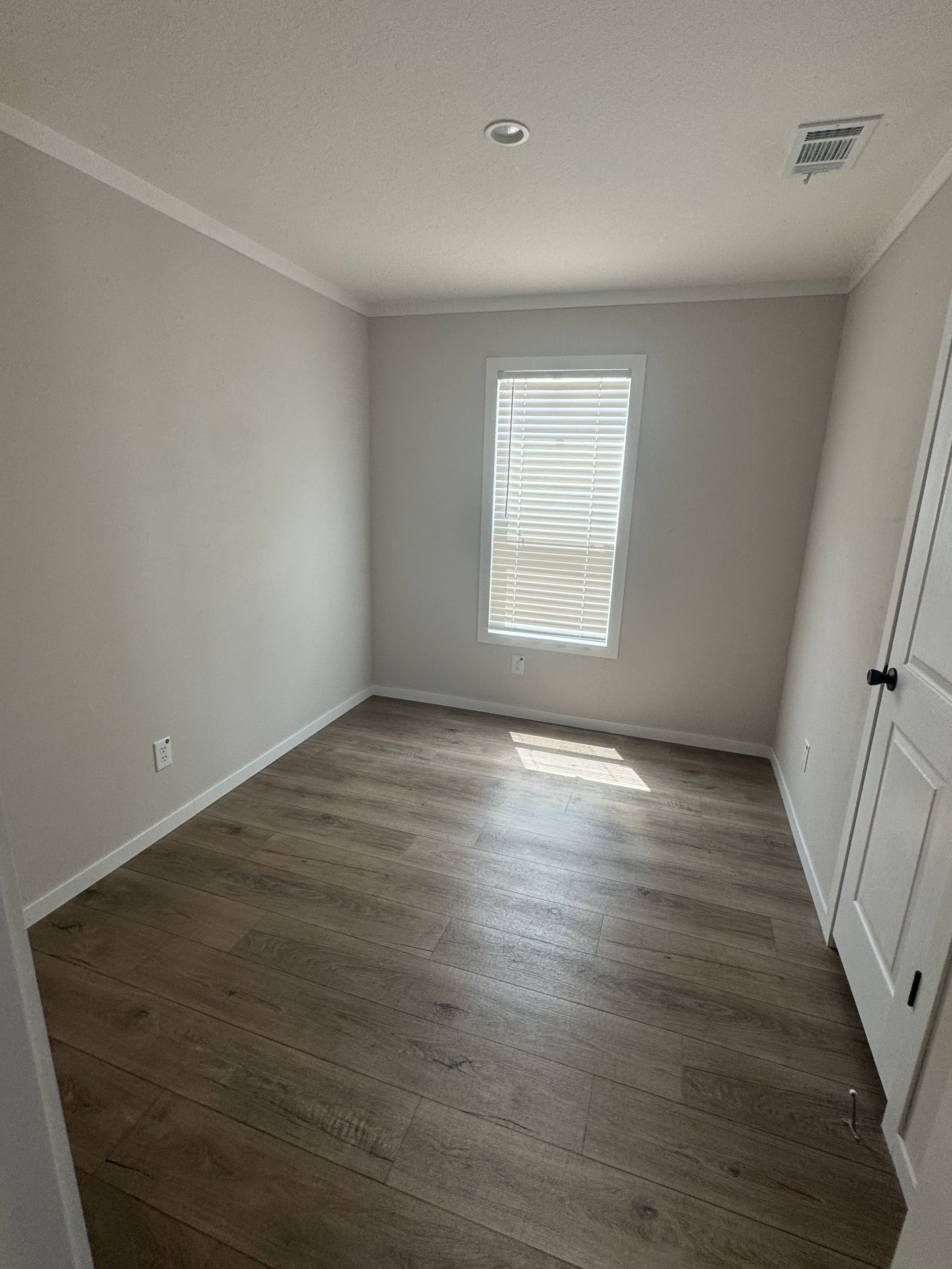 An empty bedroom with hardwood floors and a window.