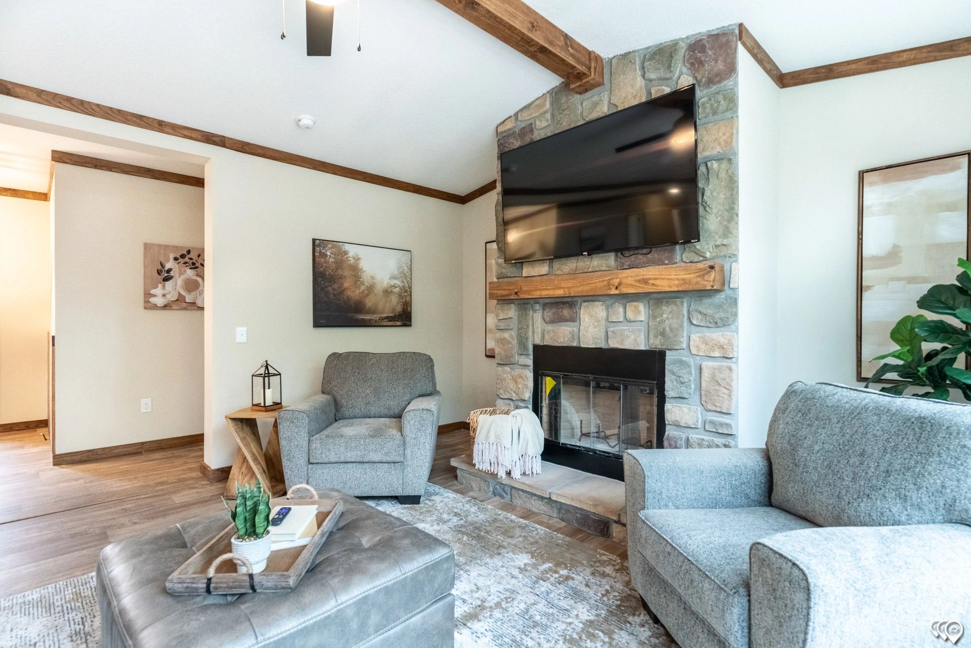 A living room with two chairs , an ottoman , a fireplace and a flat screen tv.