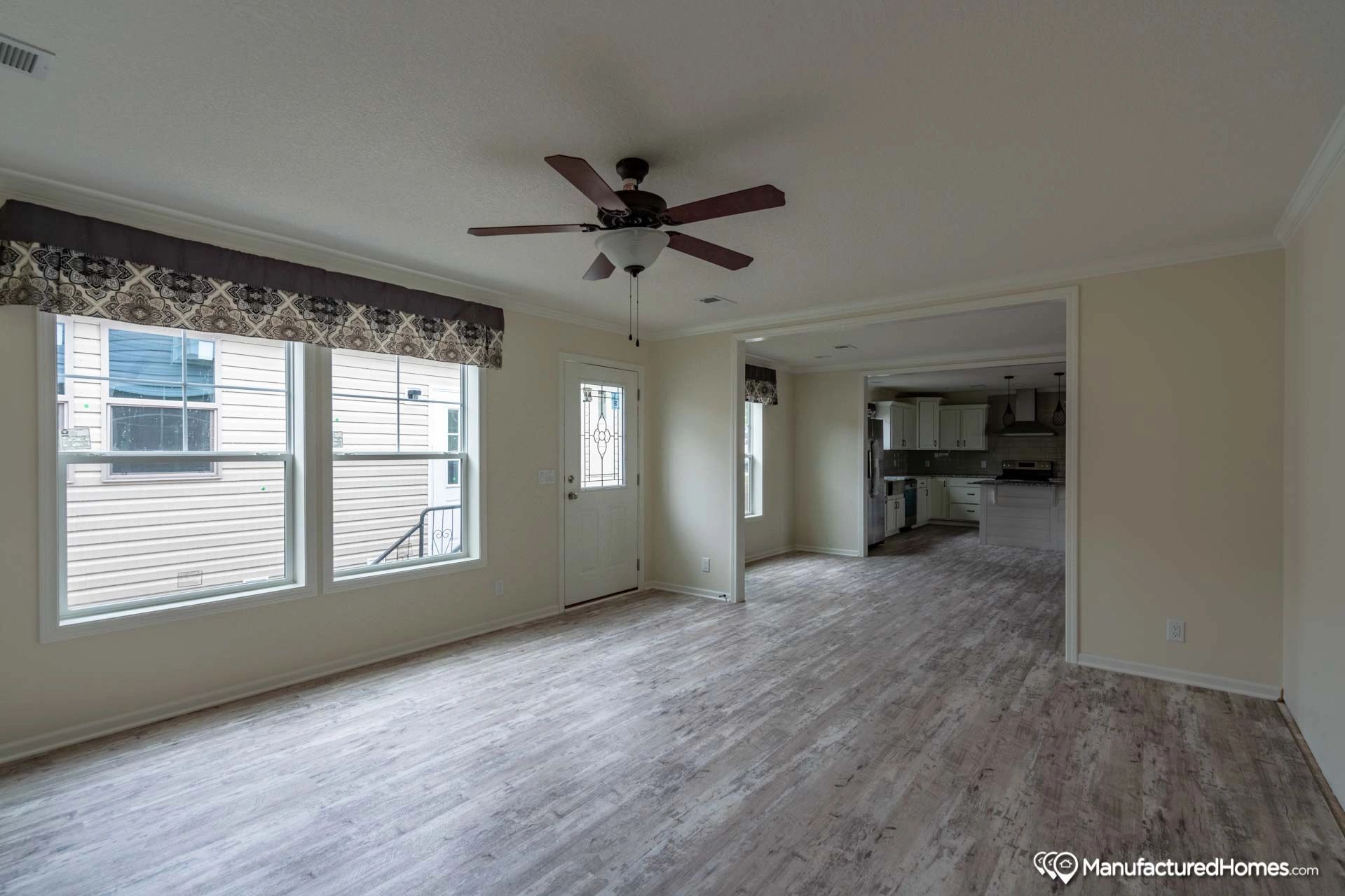An empty living room with a ceiling fan and a lot of windows.