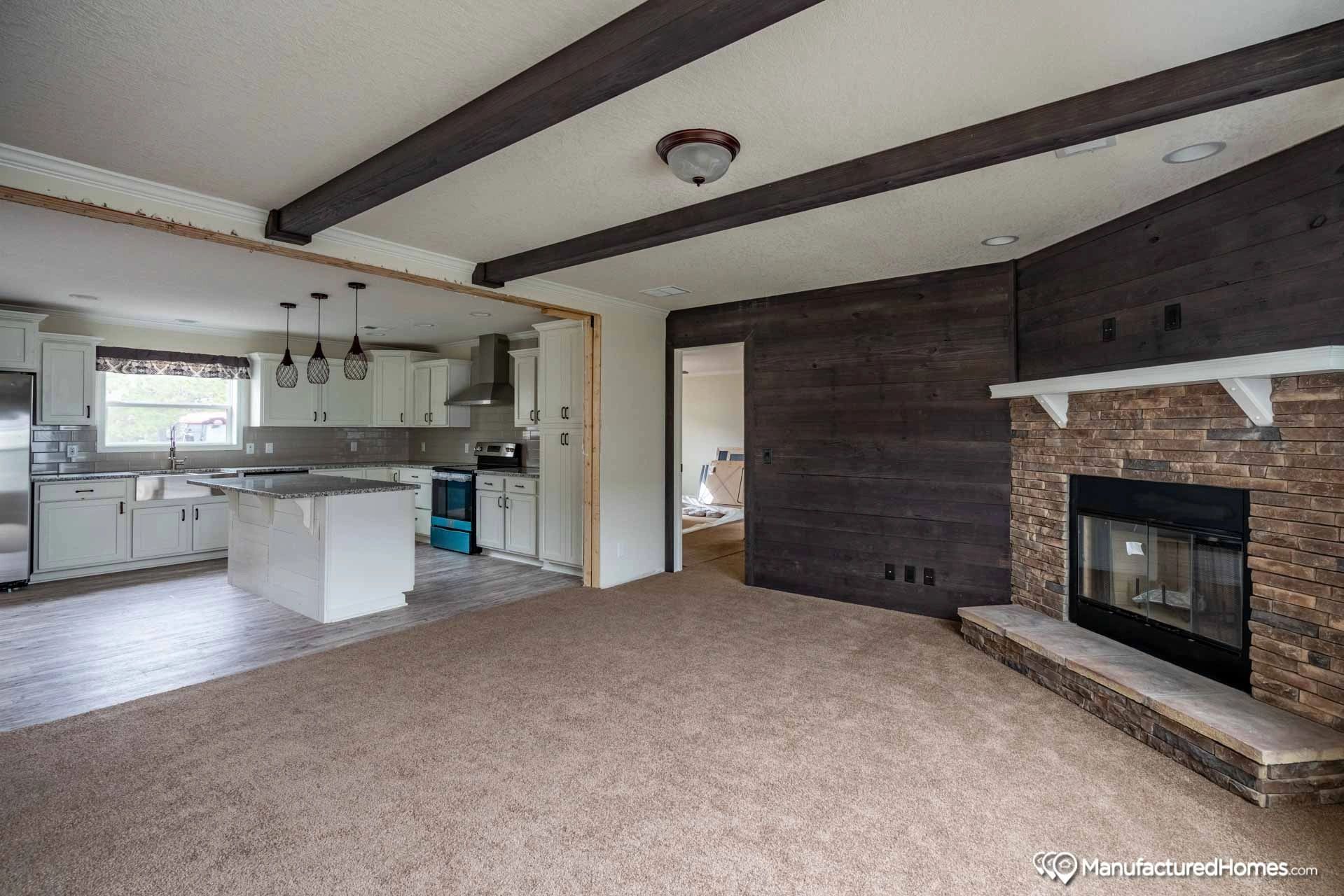 A living room with a fireplace and a kitchen in the background.