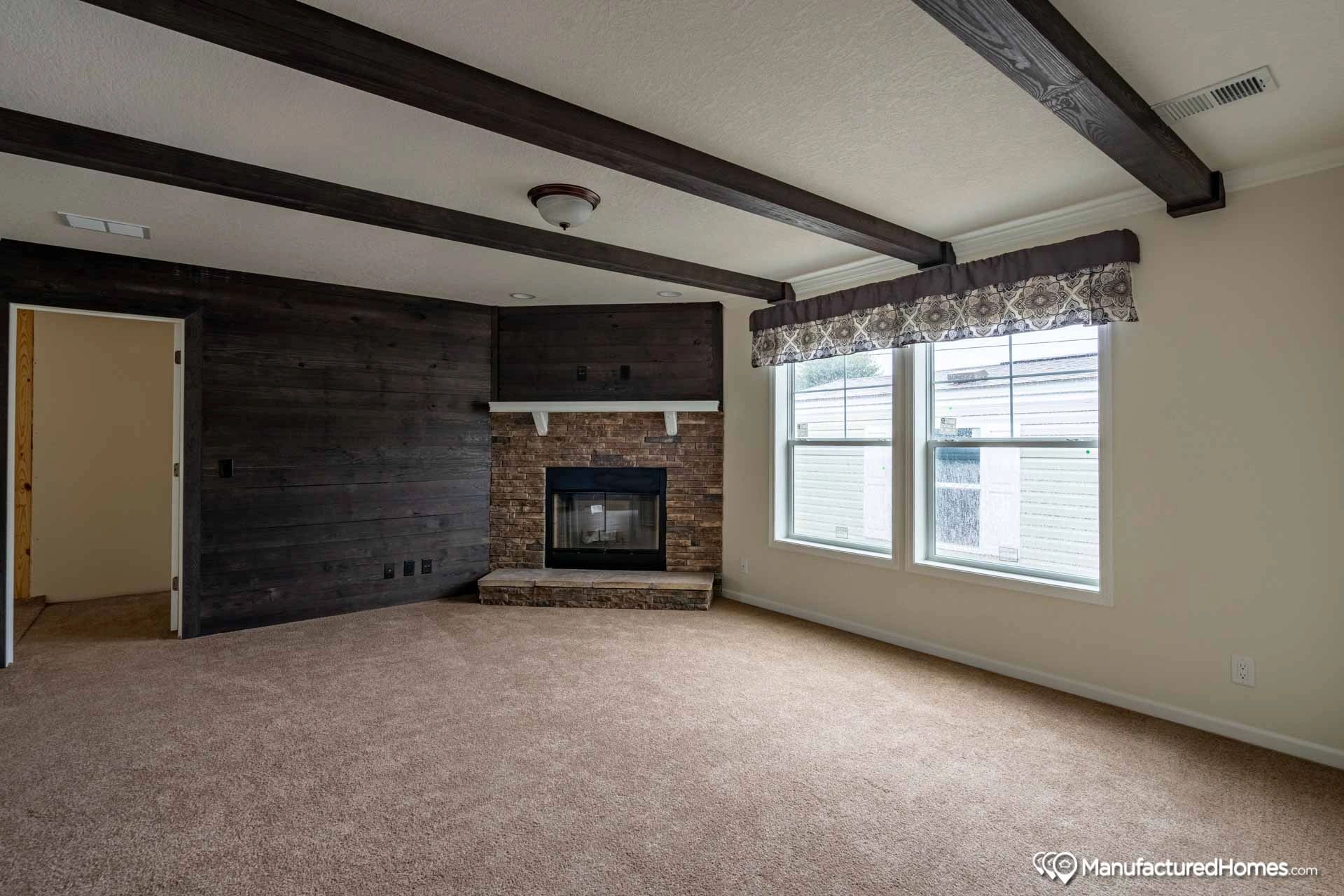 An empty living room with a fireplace and two windows.