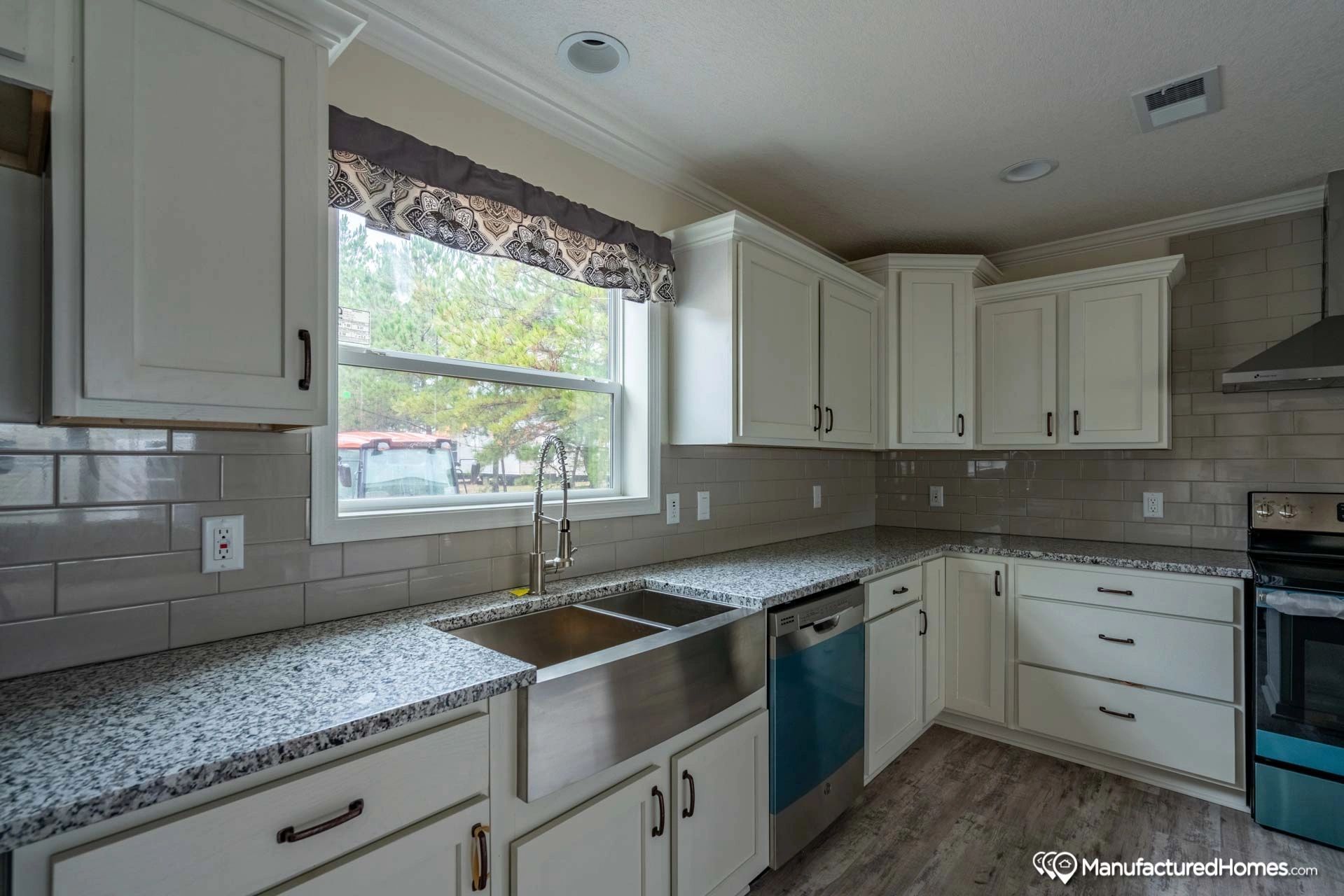A kitchen with white cabinets , granite counter tops , stainless steel appliances , a sink and a window.