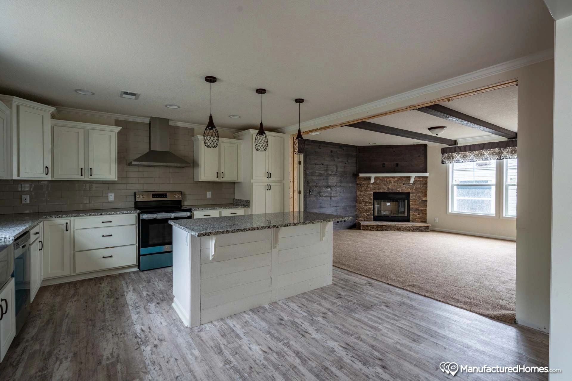 An empty kitchen with white cabinets , granite counter tops , a stove , and a fireplace.