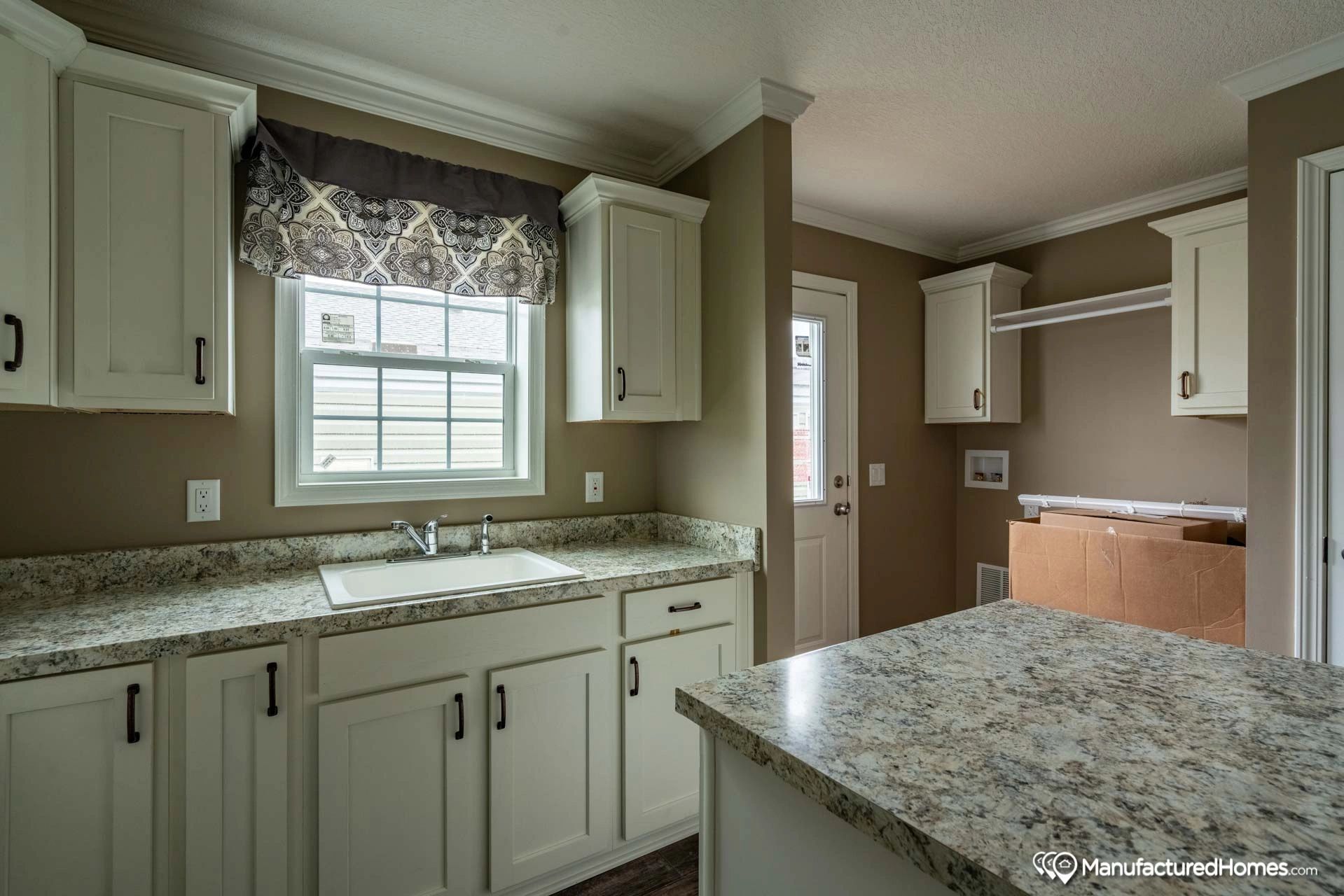 A kitchen with white cabinets , granite counter tops , a sink and a window.