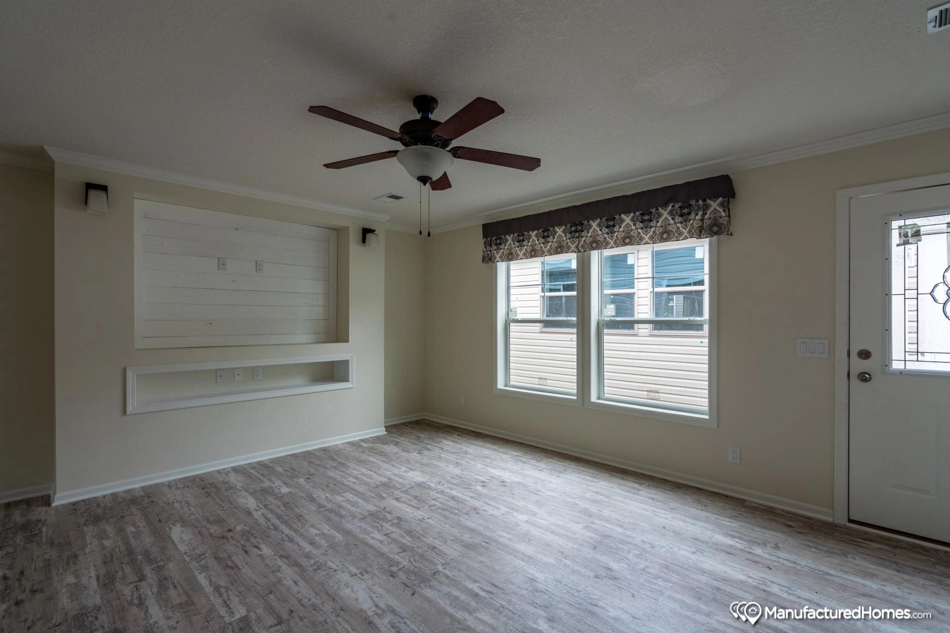 An empty living room with a ceiling fan and two windows.