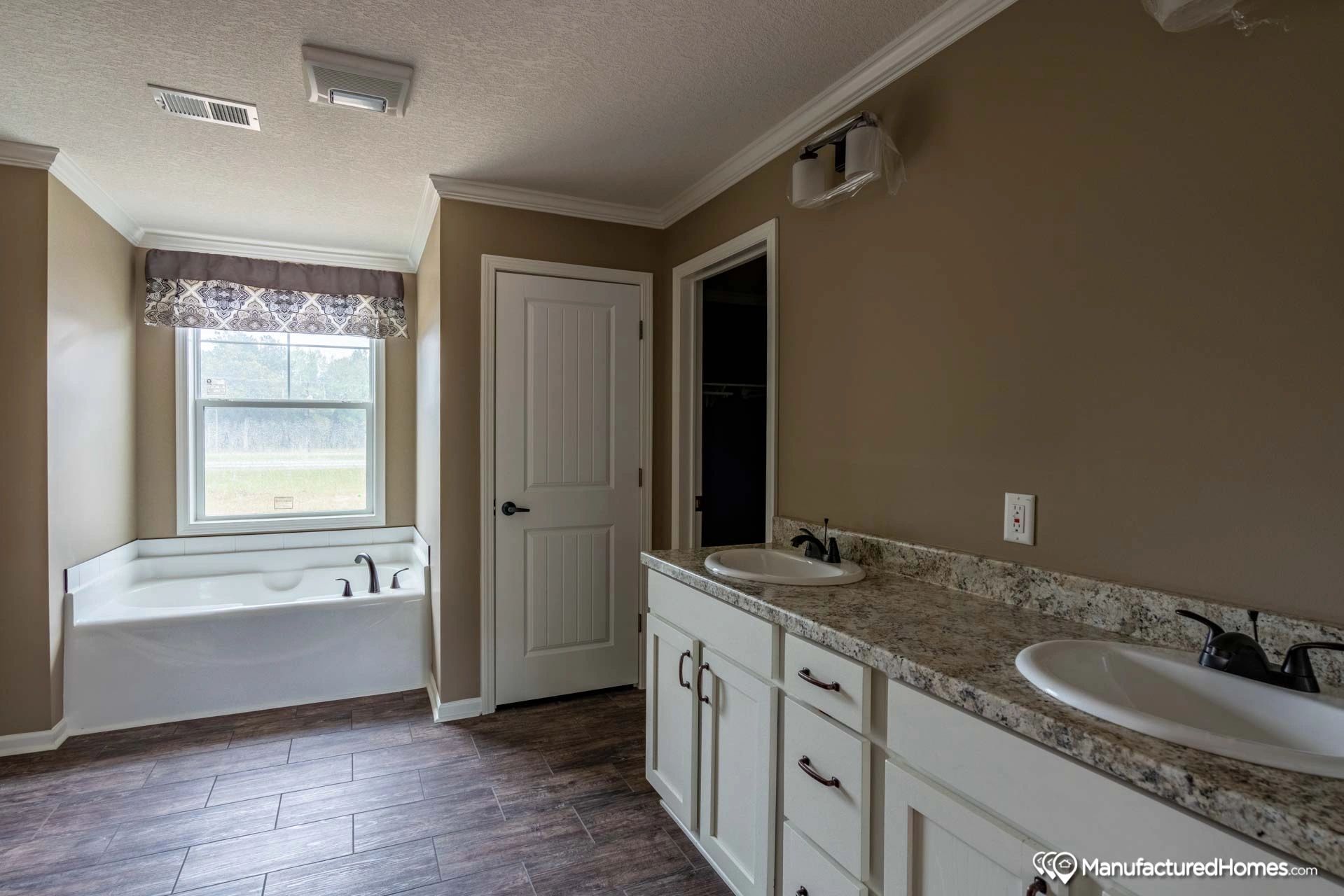A bathroom with two sinks , a tub and a window.