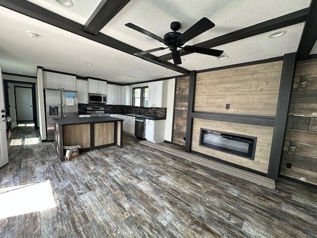A kitchen and living room in a mobile home with a fireplace and ceiling fan.