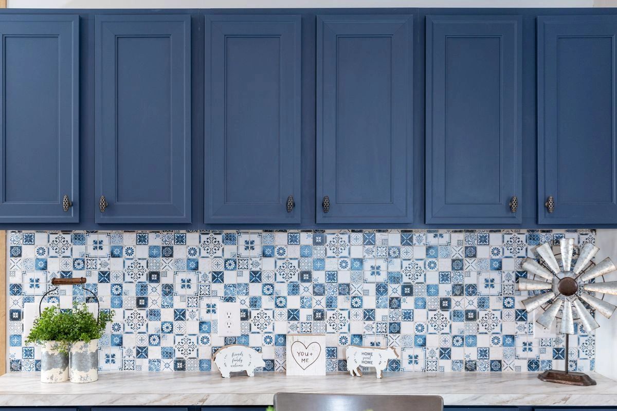 A kitchen with blue cabinets and a blue and white tile backsplash.