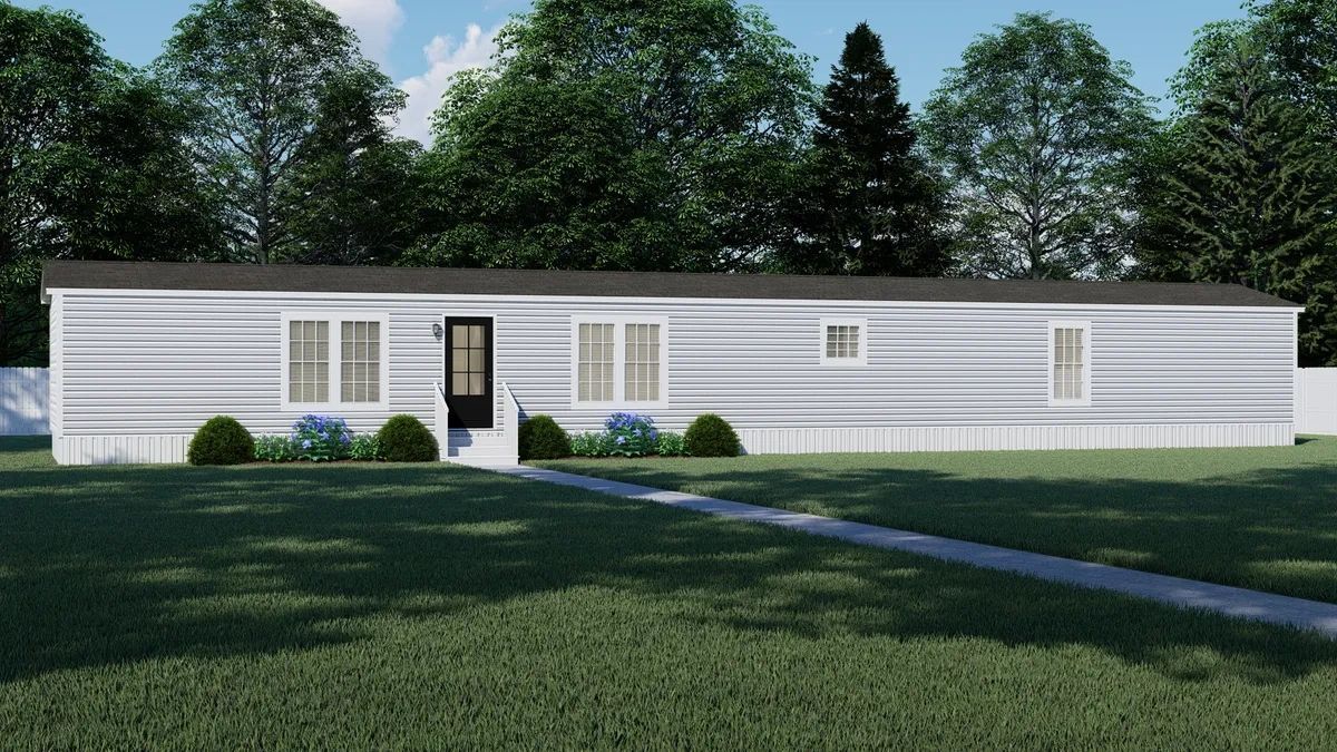 A white mobile home is sitting in the middle of a lush green field.