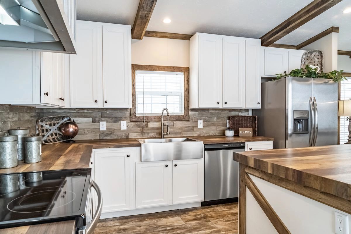 A kitchen with white cabinets , stainless steel appliances , a sink and a refrigerator.