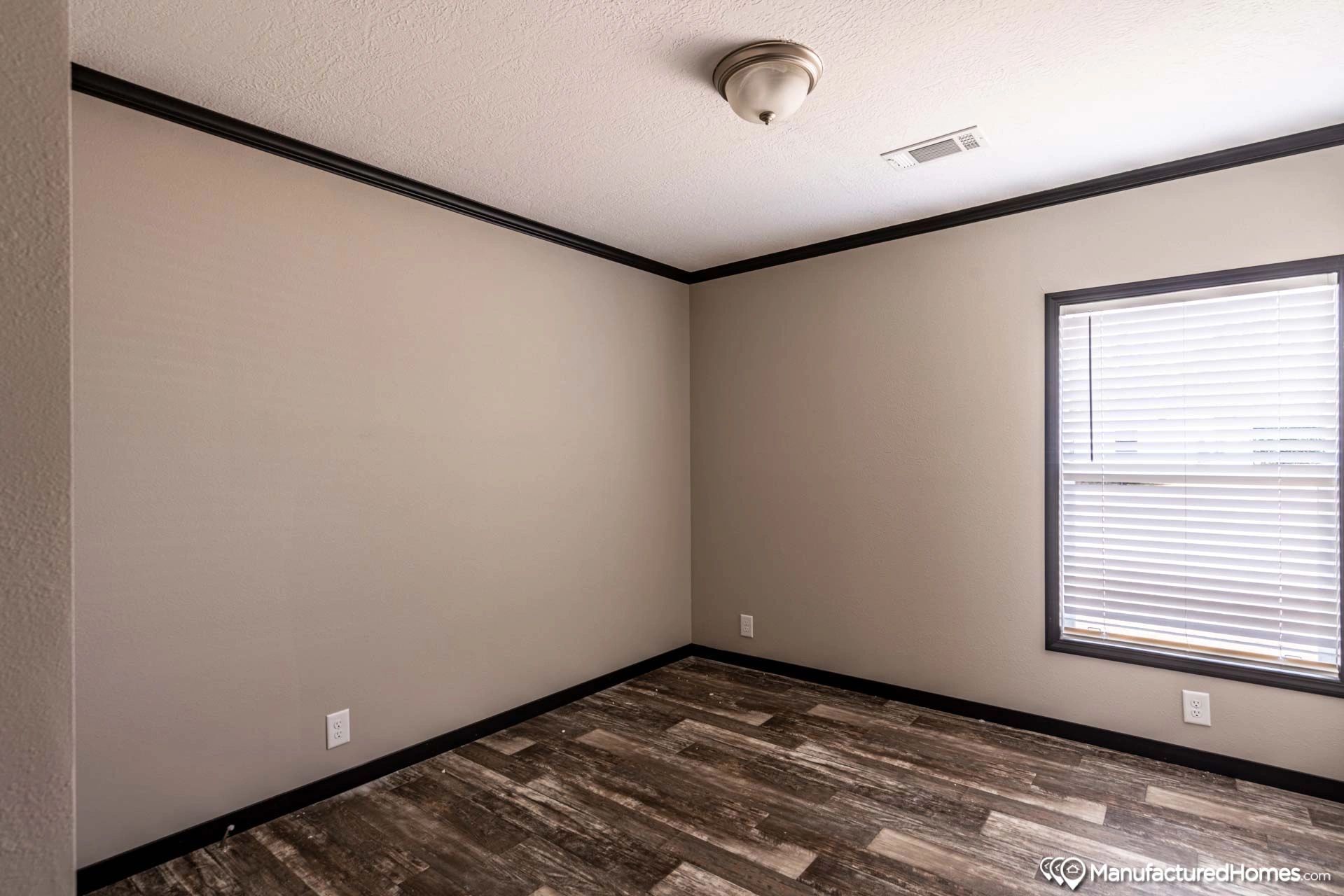 An empty bedroom with a window and a wooden floor.