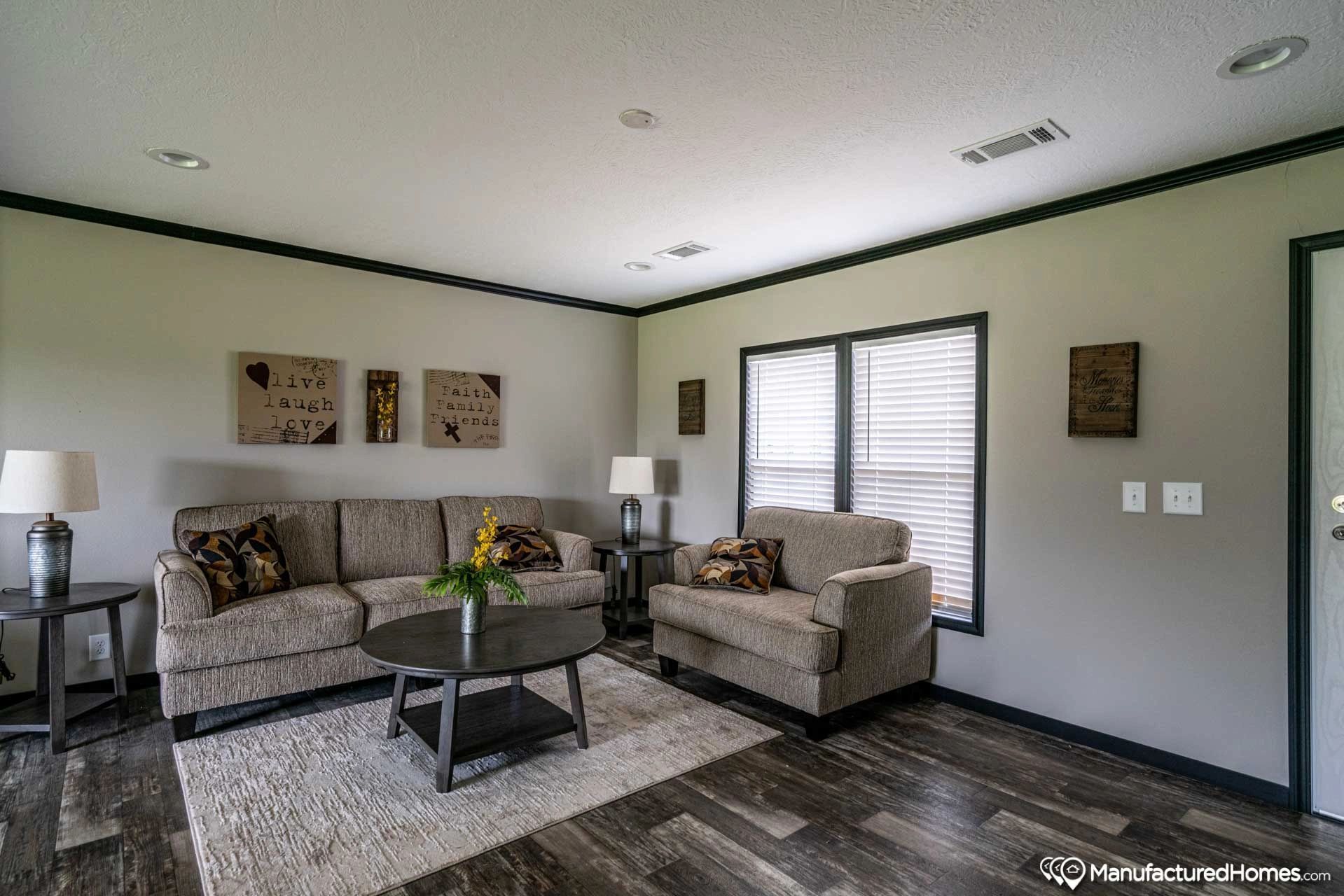 A living room with a couch , chair , coffee table and two windows.