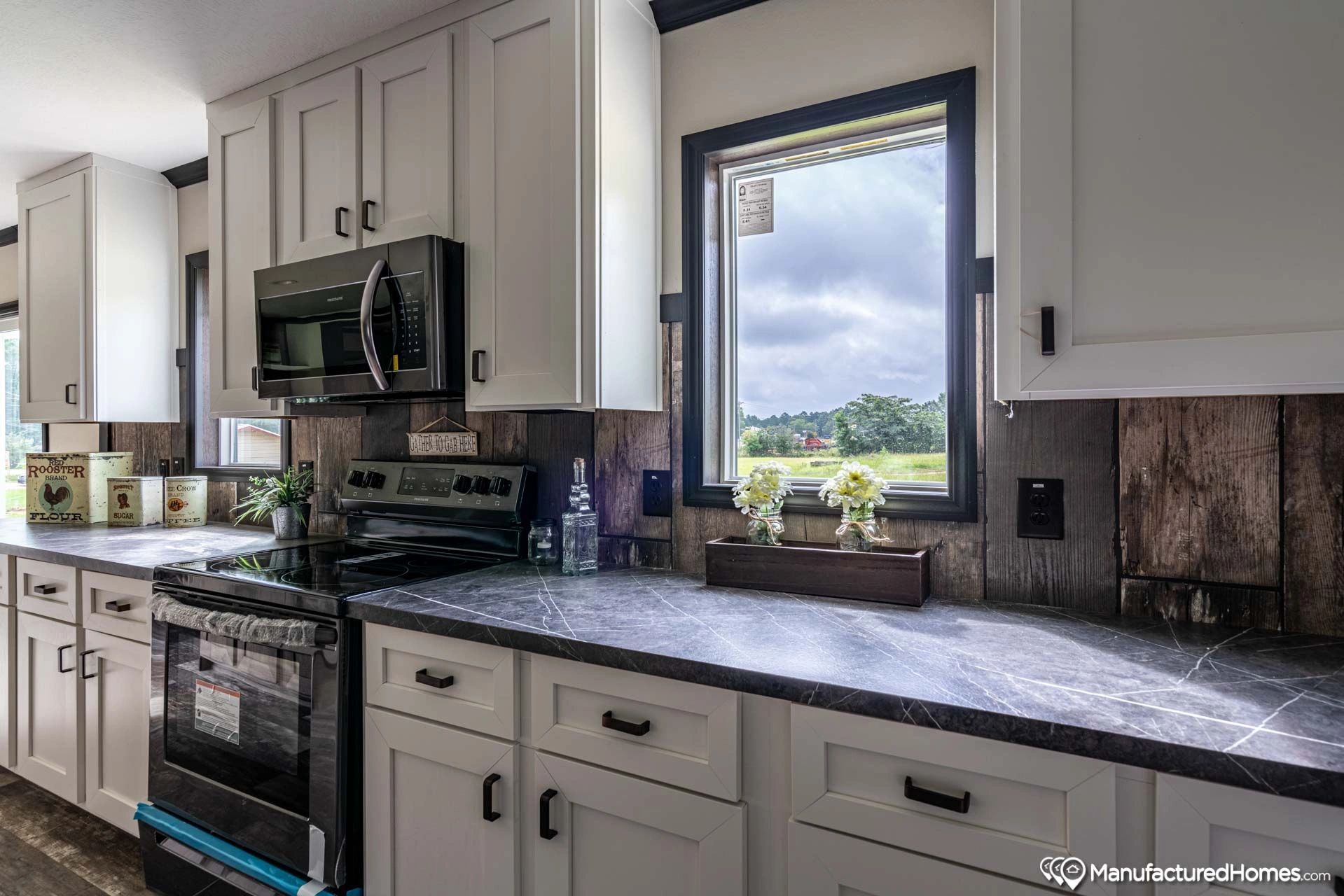 A kitchen with white cabinets , black appliances , and a window.